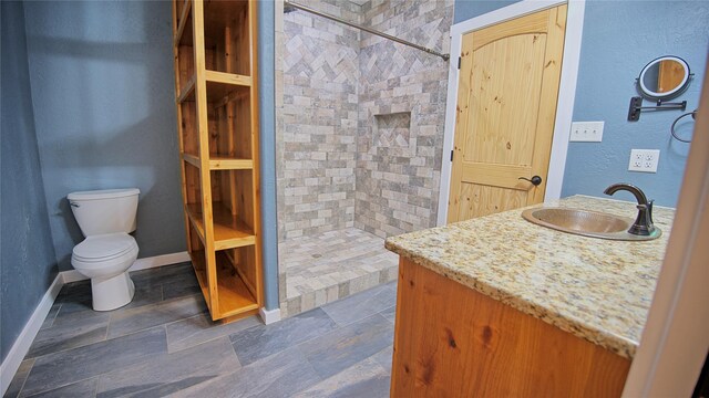 bathroom with vanity, baseboards, a tile shower, and toilet