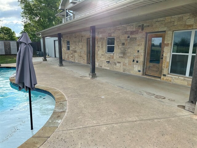 back of property with stone siding, cooling unit, an outdoor pool, a patio area, and a yard