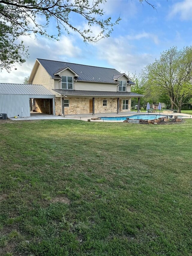 back of property with stone siding, cooling unit, an outdoor pool, a patio area, and a yard