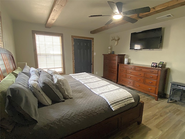 1609 Beech St, Cisco, TX 76437 - bedroom featuring light wood finished floors, beam ceiling, ceiling fan, and a wood stove