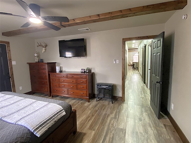 1609 Beech St, Cisco, TX 76437 - bedroom with light wood-style floors, baseboards, beam ceiling, a wood stove, and a ceiling fan