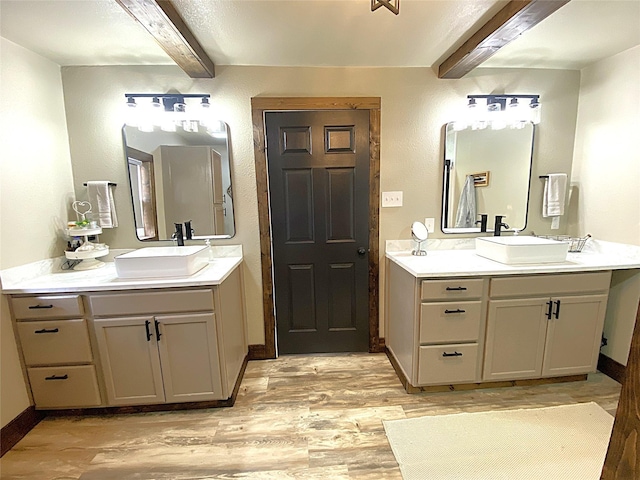 bathroom with beamed ceiling, two vanities, wood finished floors, and a sink