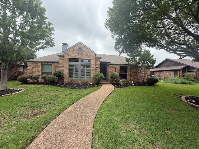 ranch-style home with brick siding, a front lawn, roof with shingles, and a chimney