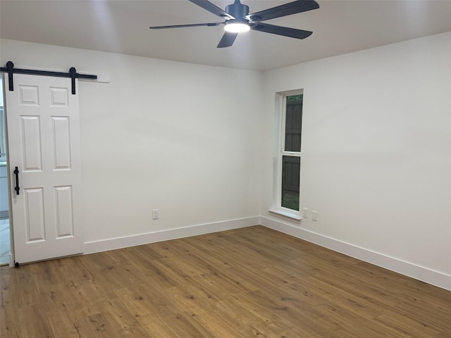 unfurnished room featuring baseboards, a barn door, and wood finished floors