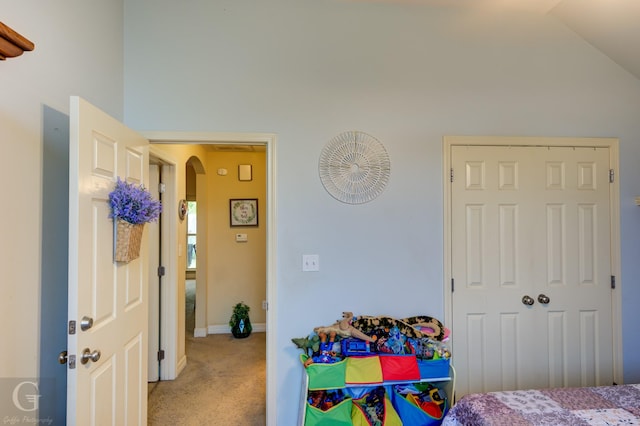 bedroom with arched walkways, vaulted ceiling, baseboards, and light carpet
