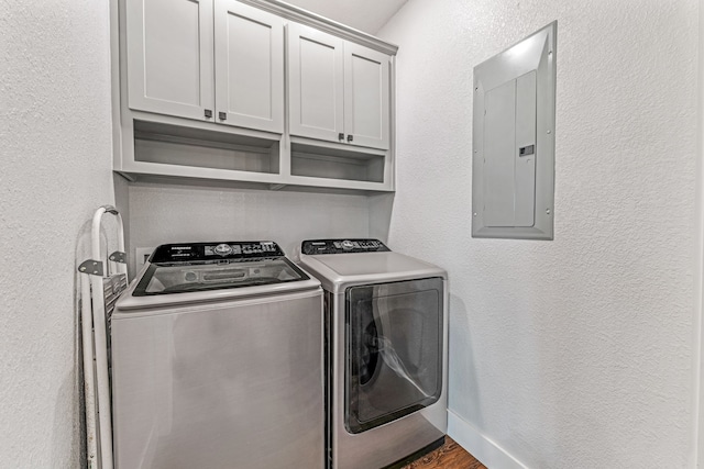 clothes washing area with washer and dryer, cabinet space, a textured wall, and electric panel