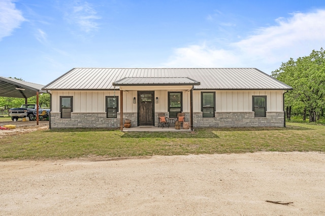 modern farmhouse featuring covered porch, stone siding, a front yard, and metal roof