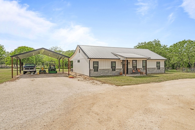 view of front of property featuring dirt driveway, a front lawn, a carport, stone siding, and metal roof