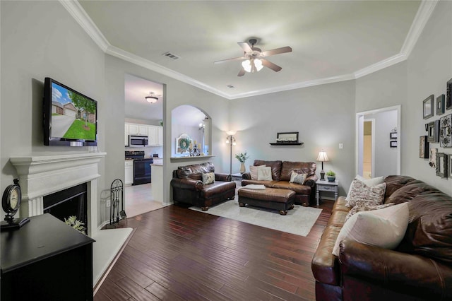 living area featuring a ceiling fan, visible vents, hardwood / wood-style flooring, a fireplace with raised hearth, and ornamental molding