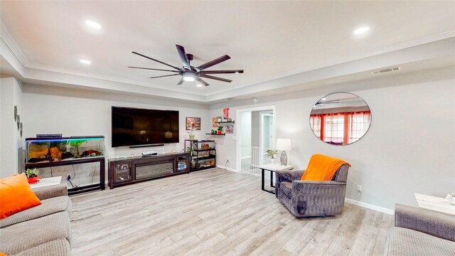 living area with a ceiling fan, visible vents, crown molding, a raised ceiling, and baseboards