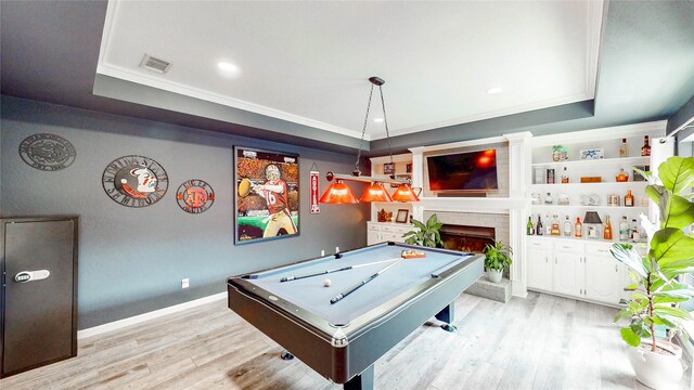game room featuring a raised ceiling, ornamental molding, a brick fireplace, and visible vents