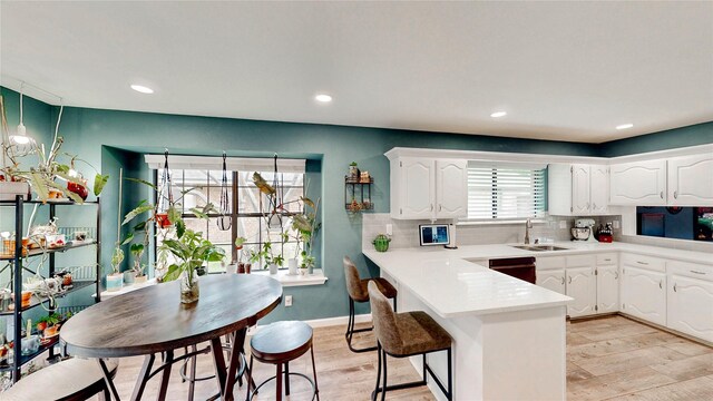 kitchen with a sink, decorative backsplash, white cabinets, and a peninsula