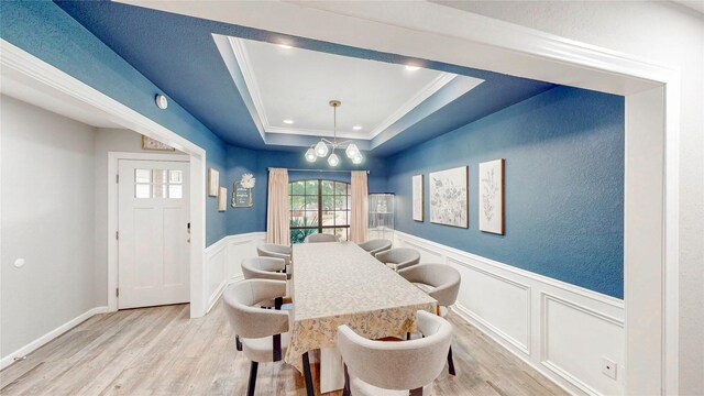 dining area featuring crown molding, a decorative wall, light wood-style floors, a wainscoted wall, and a tray ceiling