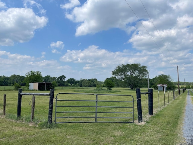 view of gate with fence, an outbuilding, a yard, and a rural view