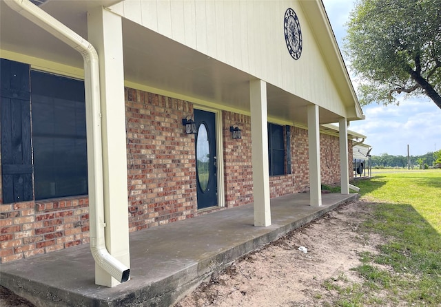 property entrance featuring a porch, brick siding, and a yard