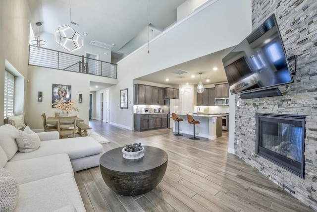living room featuring a stone fireplace, visible vents, a towering ceiling, light wood-type flooring, and baseboards