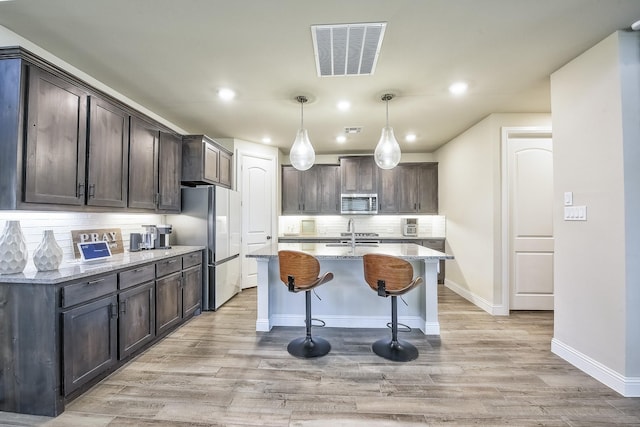 kitchen featuring visible vents, freestanding refrigerator, a kitchen bar, stainless steel microwave, and backsplash