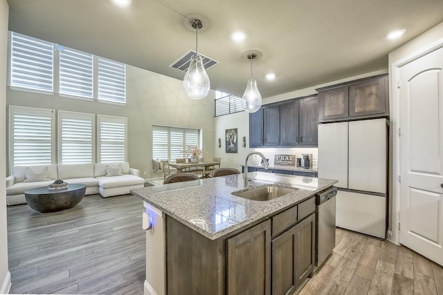 kitchen featuring freestanding refrigerator, dark brown cabinetry, a sink, light wood-style flooring, and decorative light fixtures