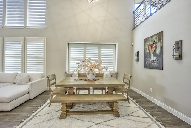 dining area featuring baseboards, a towering ceiling, wood finished floors, and a healthy amount of sunlight