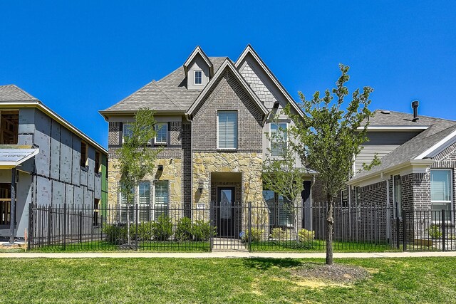 view of front of property with fence private yard, a front lawn, stone siding, brick siding, and a shingled roof