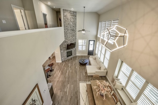 living area featuring a ceiling fan, a high ceiling, wood finished floors, and a fireplace