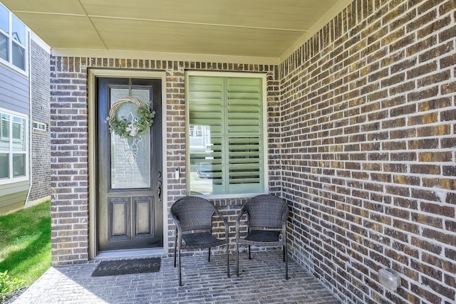 view of exterior entry with a porch and brick siding