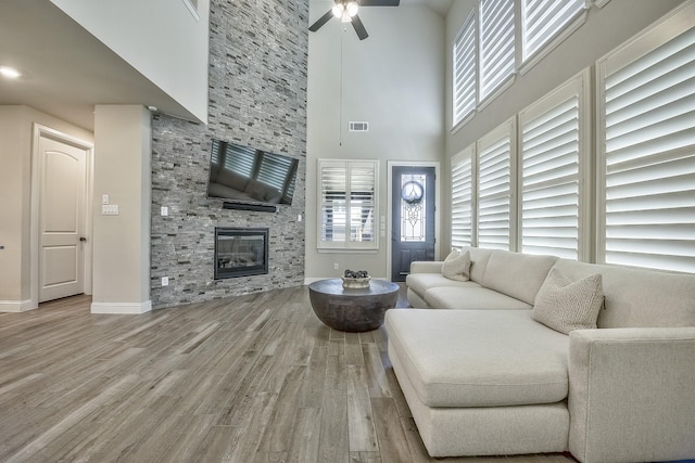 living room with a high ceiling, a stone fireplace, a ceiling fan, wood finished floors, and visible vents