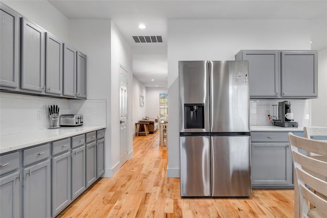 kitchen with light wood finished floors, visible vents, decorative backsplash, gray cabinets, and stainless steel fridge with ice dispenser