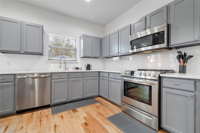 kitchen with stainless steel appliances, light countertops, a sink, gray cabinetry, and tasteful backsplash