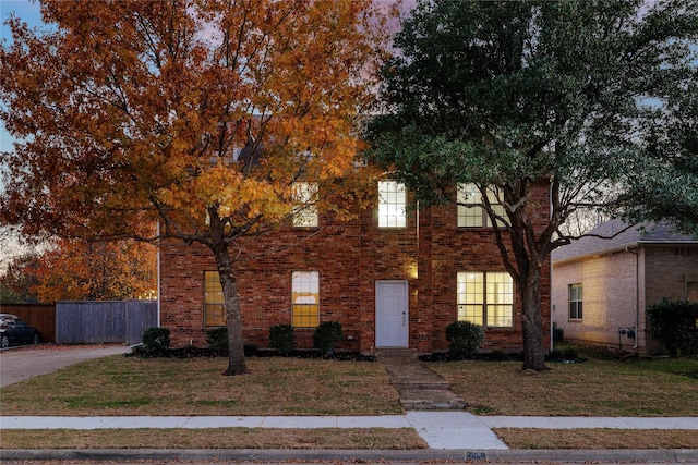 view of property hidden behind natural elements with brick siding, a front lawn, and fence