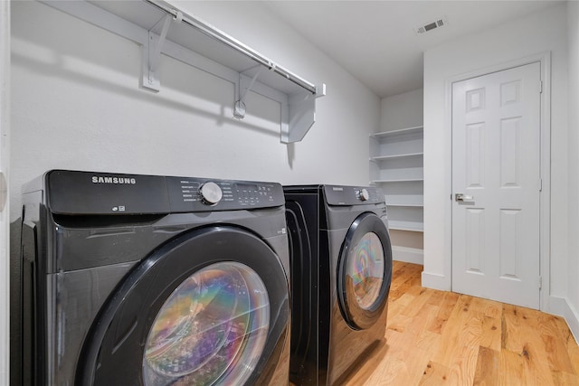 clothes washing area featuring washing machine and dryer, laundry area, light wood-style floors, and visible vents