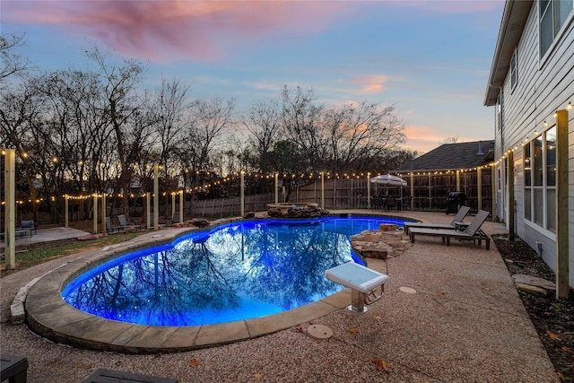pool at dusk with a fenced backyard, a patio, and a fenced in pool