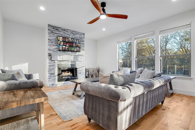 living room featuring a ceiling fan, a stone fireplace, recessed lighting, and light wood-style flooring