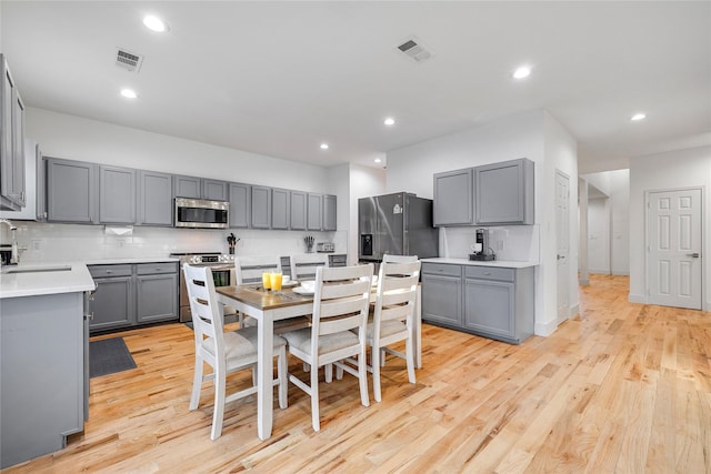 kitchen with gray cabinets, decorative backsplash, appliances with stainless steel finishes, and visible vents