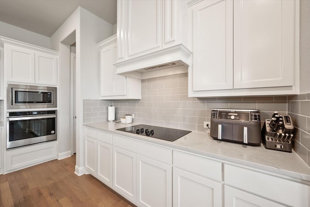 351 Evening Fire Dr, Waxahachie, TX 75167 - kitchen with white cabinets, tasteful backsplash, light wood-style floors, light stone countertops, and appliances with stainless steel finishes