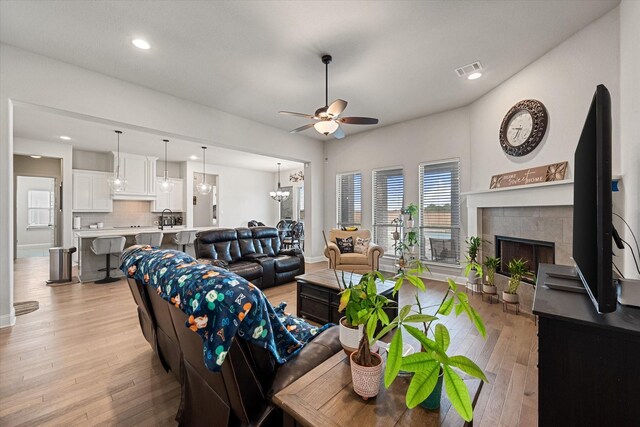 351 Evening Fire Dr, Waxahachie, TX 75167 - living room featuring a tiled fireplace, visible vents, recessed lighting, light wood-style floors, and ceiling fan with notable chandelier