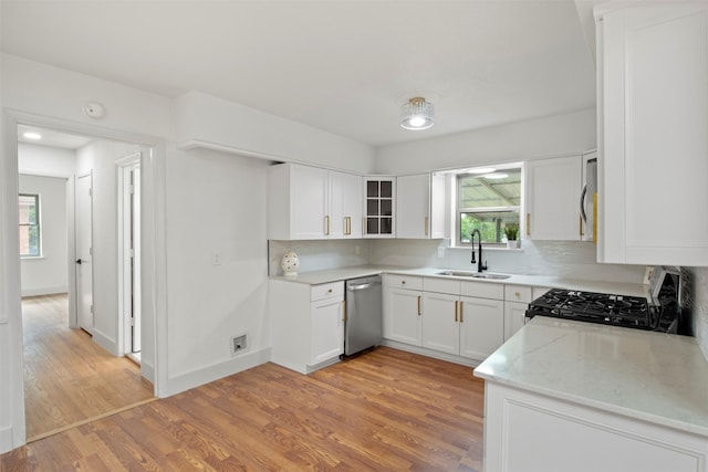 kitchen with light wood finished floors, stainless steel dishwasher, a sink, range with gas stovetop, and glass insert cabinets