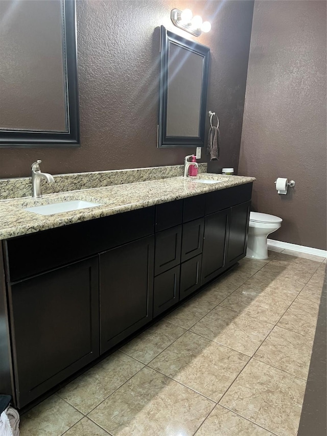 full bath with double vanity, a sink, a textured wall, and toilet