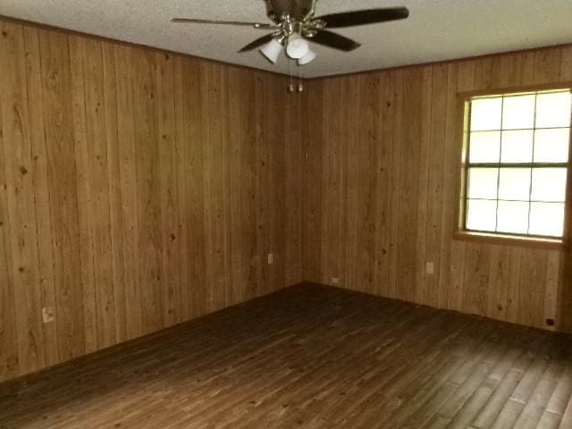 unfurnished room with wood walls, wood finished floors, and ceiling fan