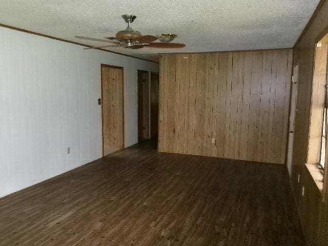 empty room featuring wooden walls, wood finished floors, a textured ceiling, and a ceiling fan