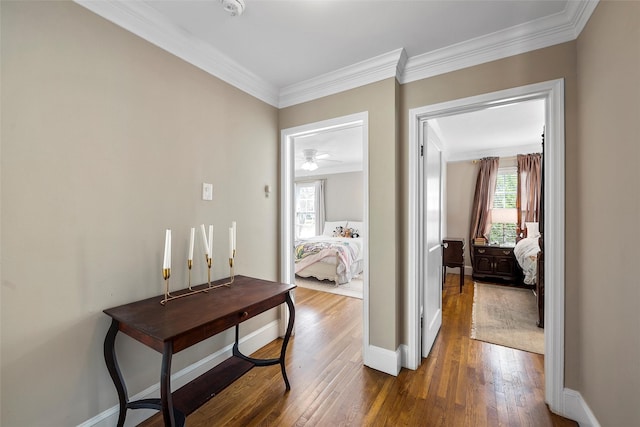 corridor featuring wood finished floors, crown molding, and baseboards
