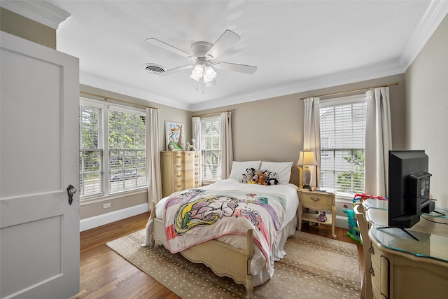 bedroom with a wood stove, wood finished floors, visible vents, and crown molding