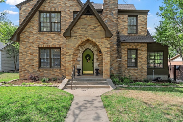 tudor home featuring brick siding, a front yard, and roof with shingles