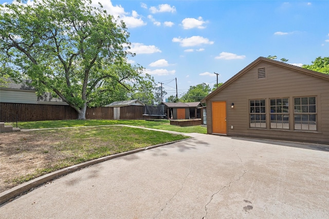 exterior space with a trampoline, a front lawn, fence, a patio, and a storage unit