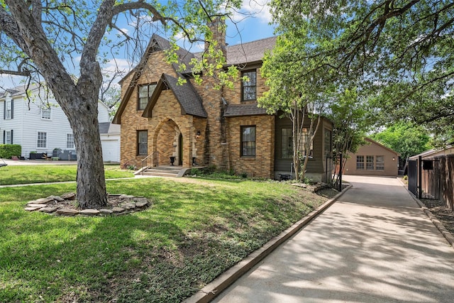 tudor home featuring a front lawn, brick siding, roof with shingles, and a chimney