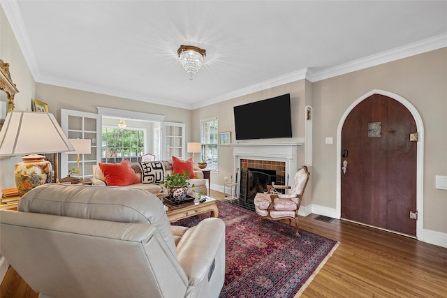 living area with arched walkways, visible vents, wood finished floors, a tile fireplace, and ornamental molding