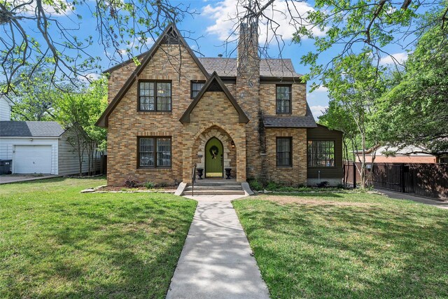 tudor-style house featuring brick siding, a front lawn, and fence