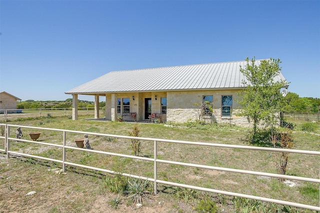 exterior space with an exterior structure, stone siding, a rural view, metal roof, and stucco siding