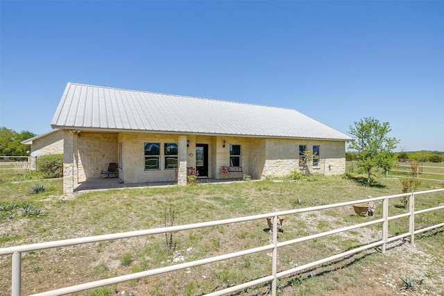 ranch-style home with stone siding, a patio area, fence, and metal roof