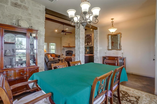 dining space featuring a stone fireplace, vaulted ceiling with beams, baseboards, finished concrete flooring, and ceiling fan with notable chandelier